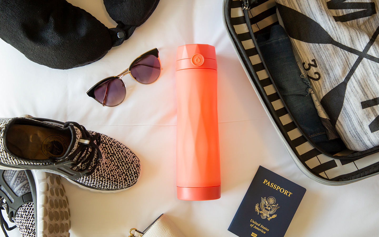 coral orange hidratespark 3 laying on bed with other traveling items scattered around.