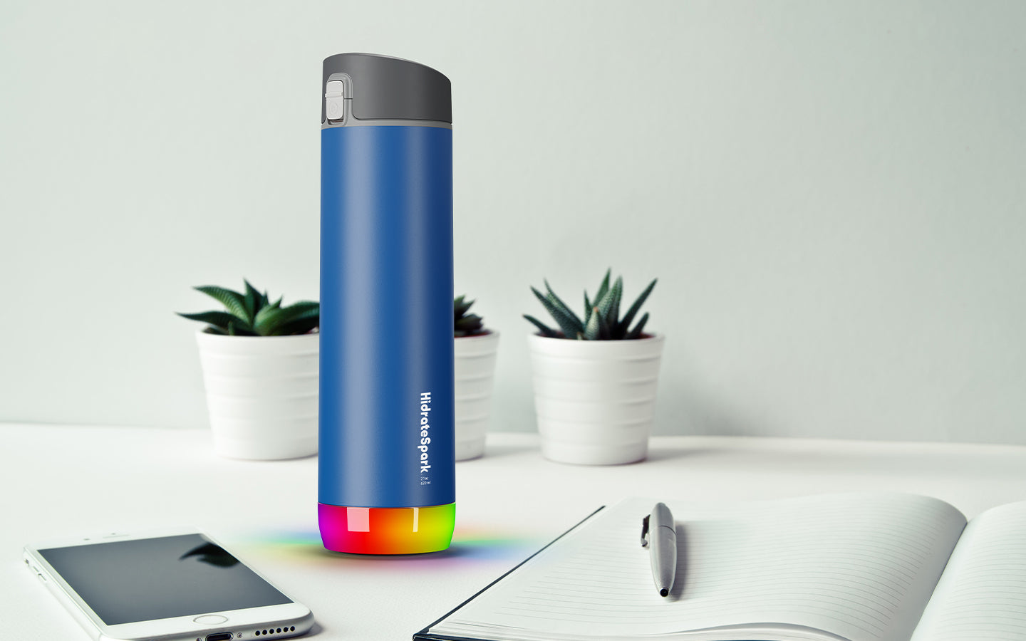 storm gray colored hidratespark 3 bluetooth smart water bottle laying on table with office items.