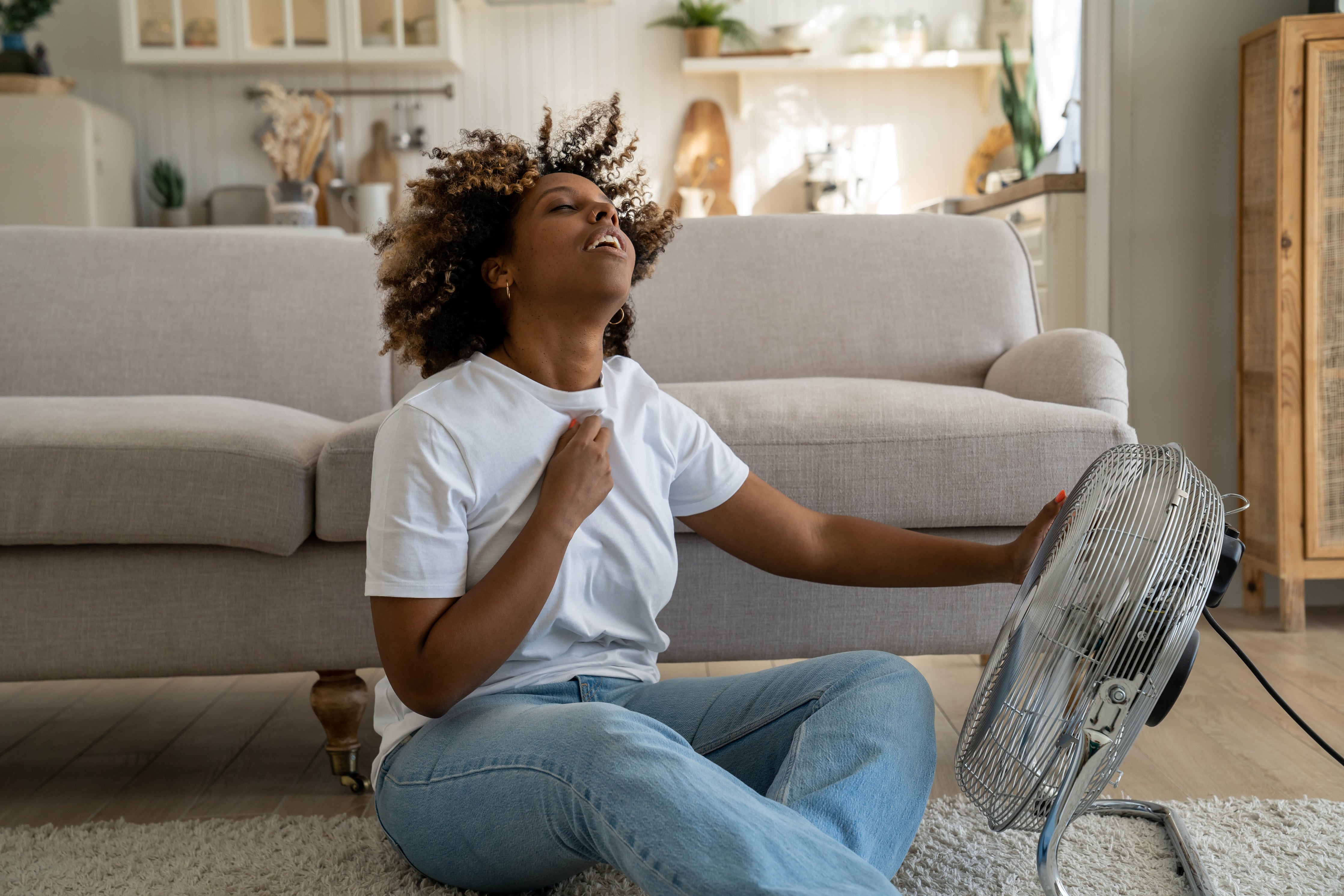 A woman using a fan wondering how to stay hydrated in hot weather.