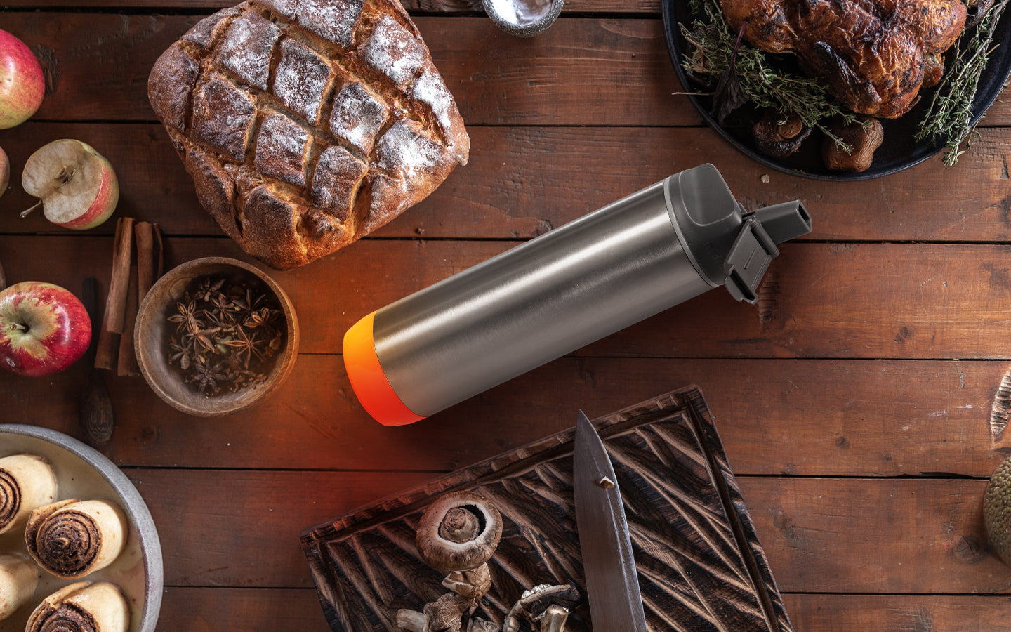 A 21 oz insulated Stainless Steel HidrateSpark PRO Bottle with a straw cap lays flat on a table surrounded by Thanksgiving foods.
