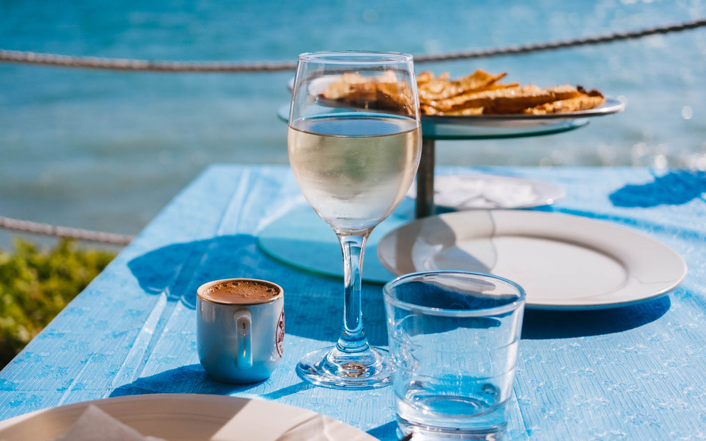 Glasses of wine, coffee, and water sit on a table with snacks in the background